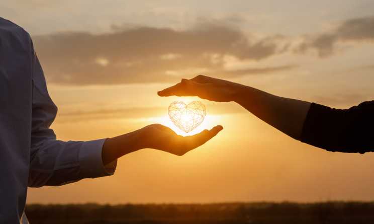 Ab wann ist man in einer Beziehung: Zwei Händen strecken sich entgegen und halten im Inneren ein Herz, das von der Sonne beleuchtet wird.